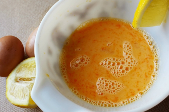 White bowl of yellow sauce with egg shells and lemon on the counter